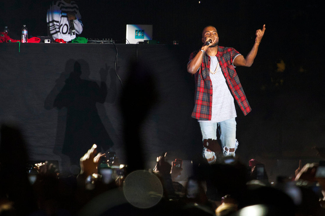 Kanye West performing with a microphone and red plaid shirt onstage at the 2013 Odd Future Carnival