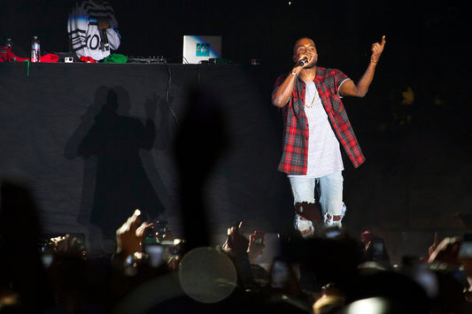 Kanye West performing with a microphone and red plaid shirt onstage at the 2013 Odd Future Carnival
