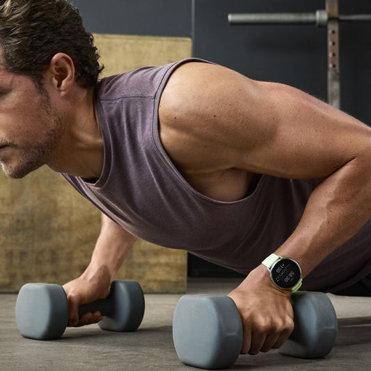 A man performing a dumbbell-supported push-up in a gym while wearing a fitness smartwatch