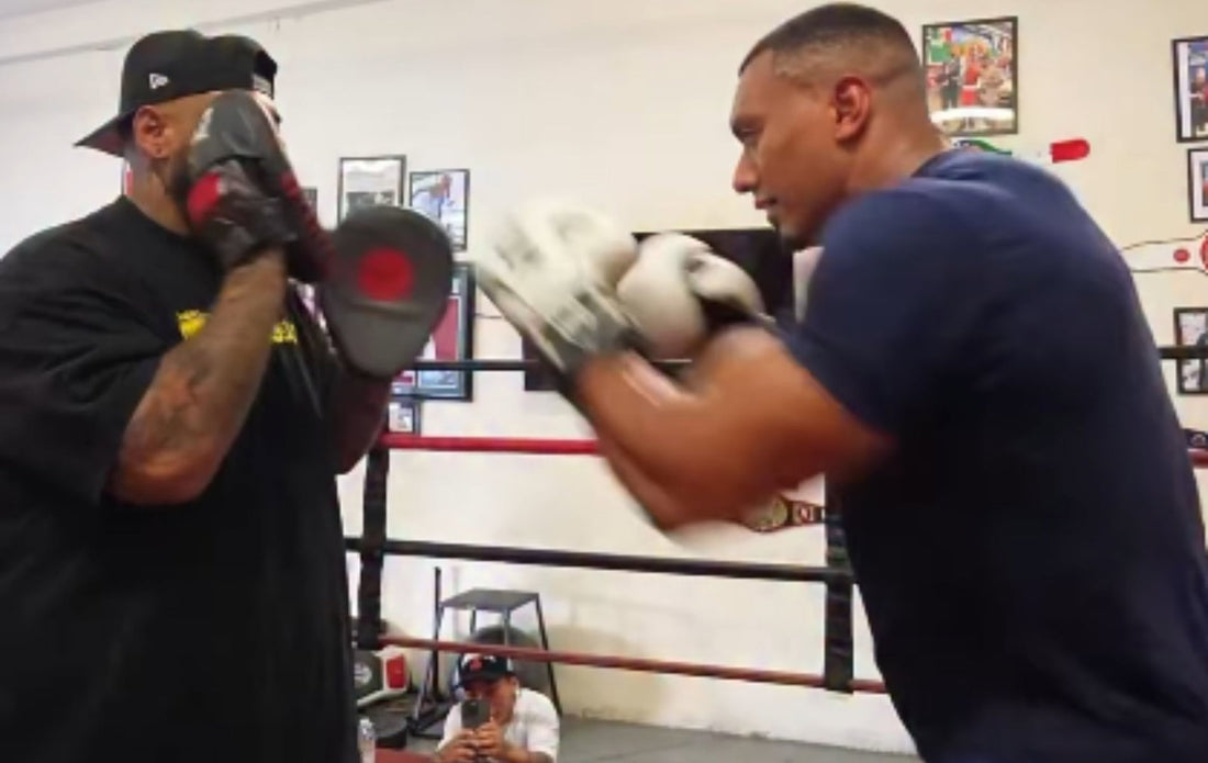 Larry Wheels wearing white boxing gloves and throwing a punch toward a trainer's mitts in a boxing gym