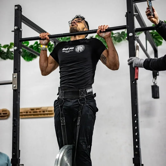 Male athlete performing a heavy weighted pull-up with a weight plate hanging from a dip belt in a gym.