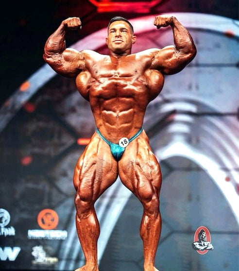 Derek Lunsford posing onstage with a muscular Mr. Olympia physique