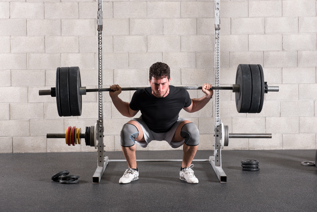 Male lifter performing a demanding barbell back squat inside a gym rack