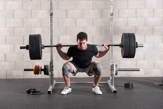 Male lifter performing a demanding barbell back squat inside a gym rack