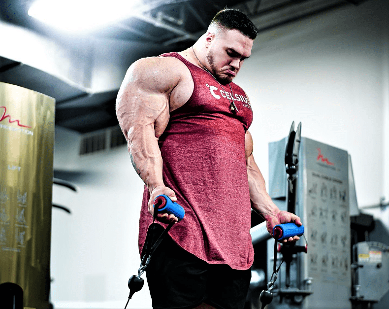 Nick Walker doing controlled cable curls in a bodybuilding gym