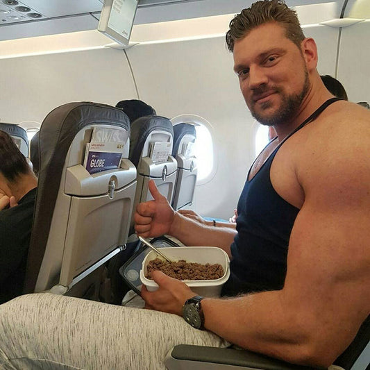 Olivier Richters seated on an airplane holding a prepared meal container and giving a thumbs-up