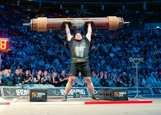 Ondřej Fojtů pressing a heavy strongman log overhead in a packed arena