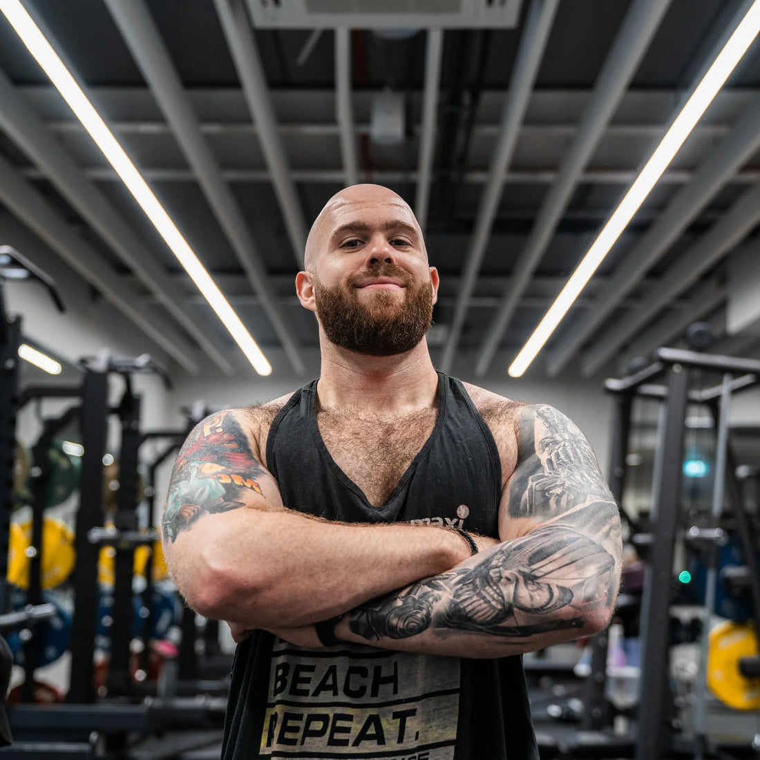 Dr. Pak standing in a gym with tattooed arms crossed, wearing a black tank top