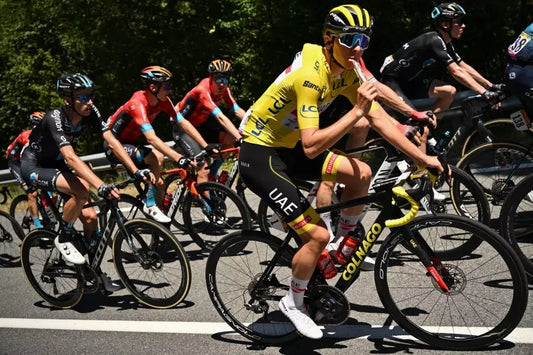 Professional road cyclist in a yellow race jersey eating an energy gel while riding among a peloton