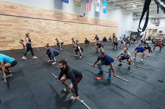 Group functional-fitness class performing synchronized barbell squat drills in a spacious gym