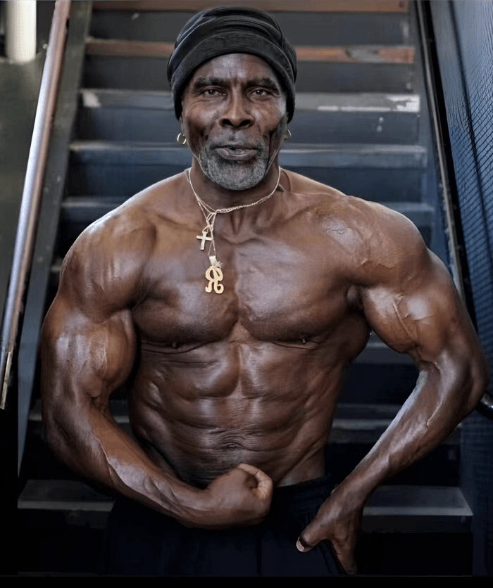 Older Robby Robinson flexing his chest and arms in a gym