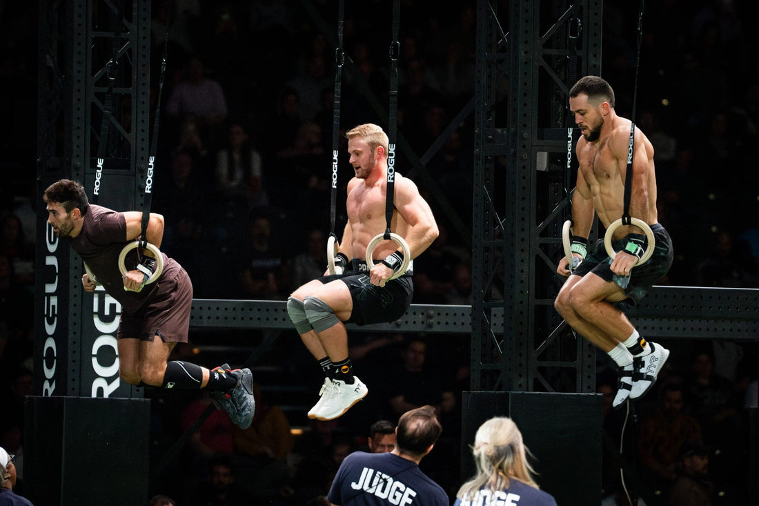 CrossFit athlete performing a controlled ring muscle-up above wooden gymnastics rings