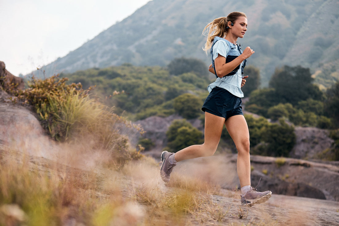 Runner wearing open-ear headphones on a rocky outdoor trail