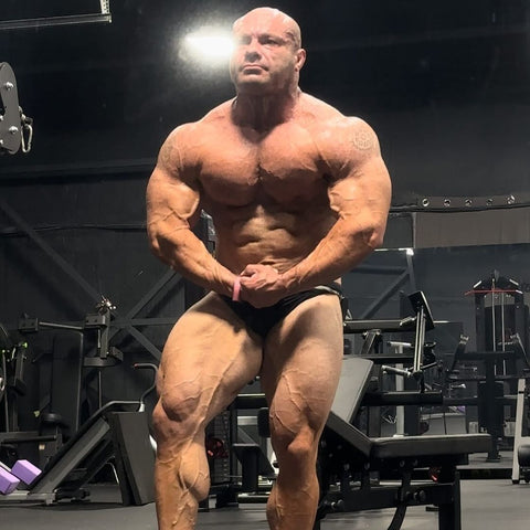 Mike Israetel flexing his chest, shoulders, arms and legs in a gym posing stance