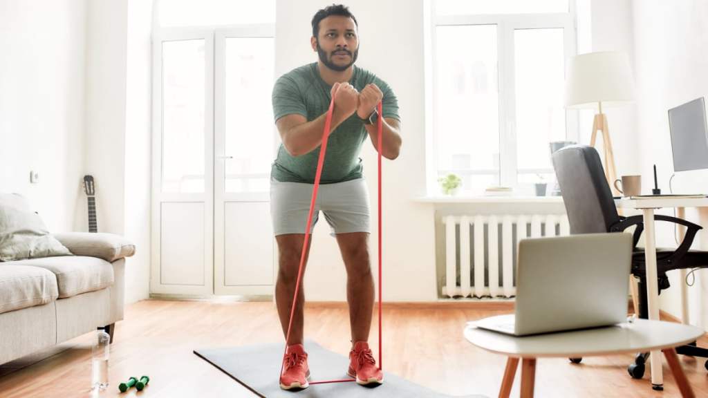 Man using a red resistance band for a standing exercise in a bright home workout space