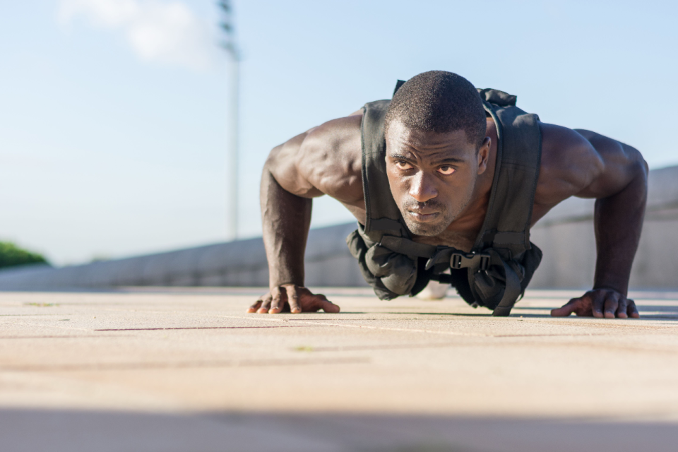 Muscular man performing an outdoor push-up while wearing a dark weighted vest
