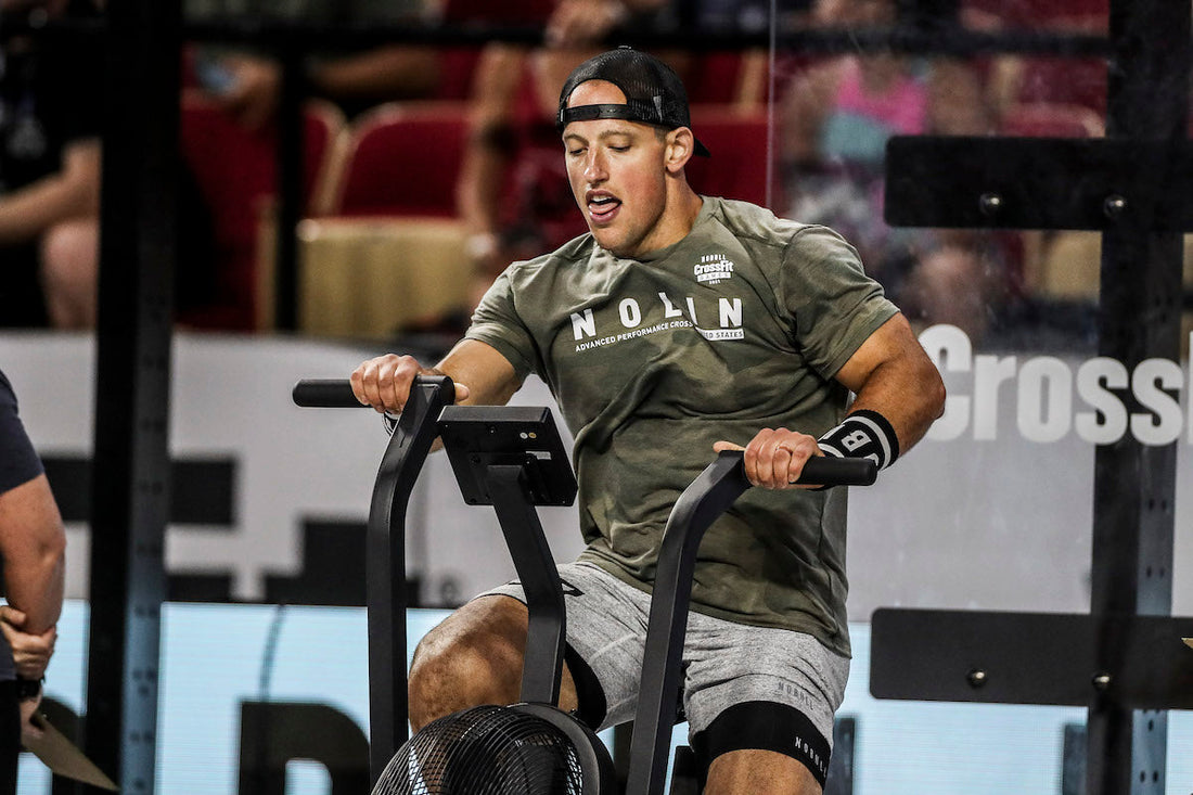 A CrossFit athlete driving the handles and pedals of a fan air bike during a hard interval