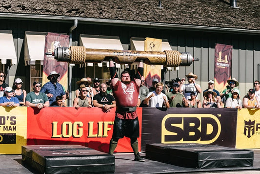 Trey Mitchell hoisting a heavy wooden log overhead at a strongman competition