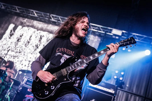 Death metal guitarist performing under blue stage lights at a live extreme-metal concert.
