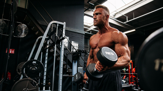 Muscular man performing a controlled dumbbell biceps curl in a gym