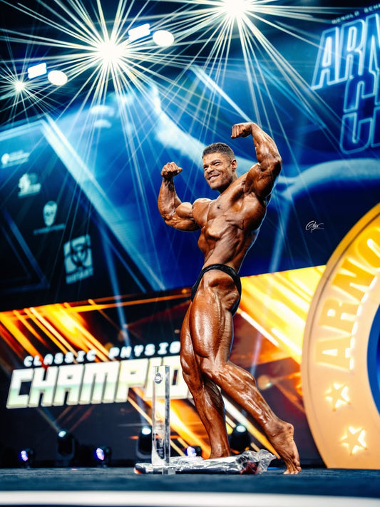 Wesley Vissers poses on the 2026 Arnold Classic stage with arms flexed under blue stage lighting