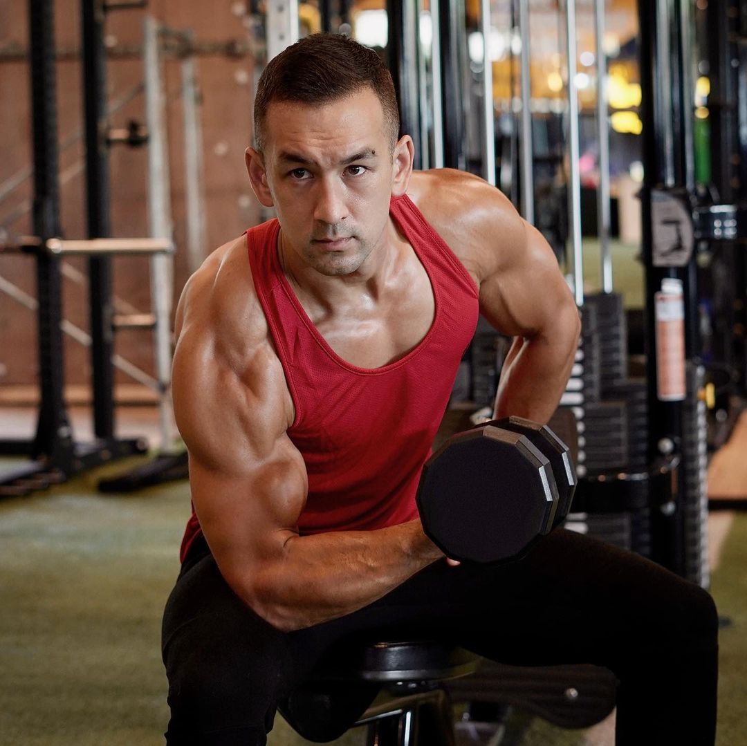Sean Nalewanyj performing a one-arm dumbbell row in a red tank top inside a gym