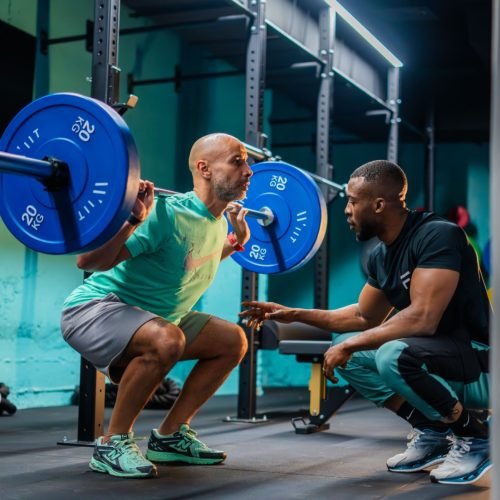 Personal trainer coaching a lifter through a loaded barbell squat in a gym