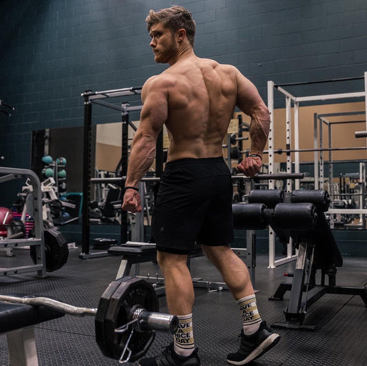Jeff Nippard showing his developed back in a gym beside a loaded barbell.