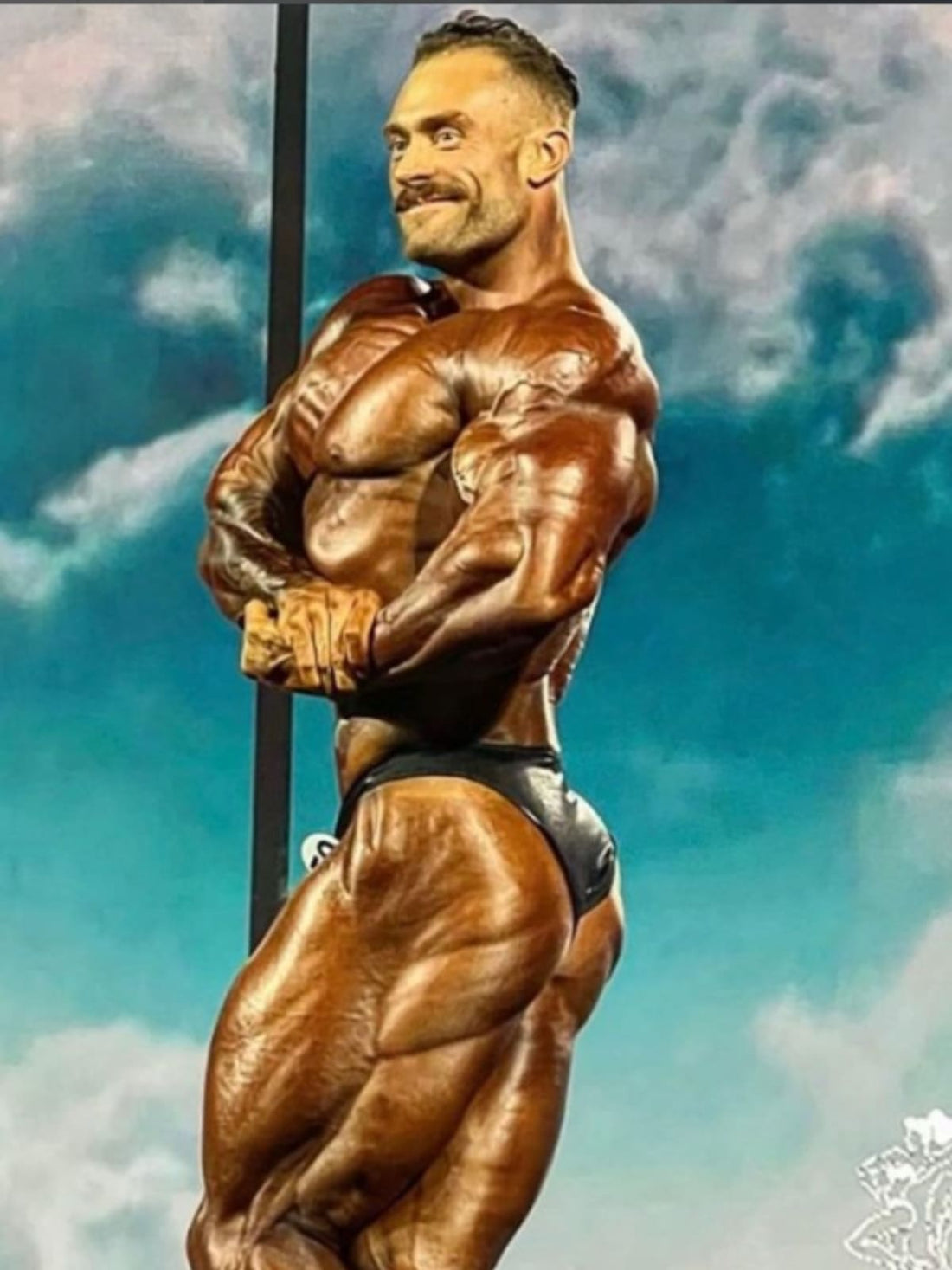 Chris Bumstead standing in a front Classic Physique Olympia pose, displaying prominent upper-chest and shoulder development