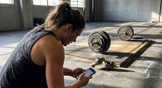 An athlete checks a workout tracking app beside a loaded barbell in a gym