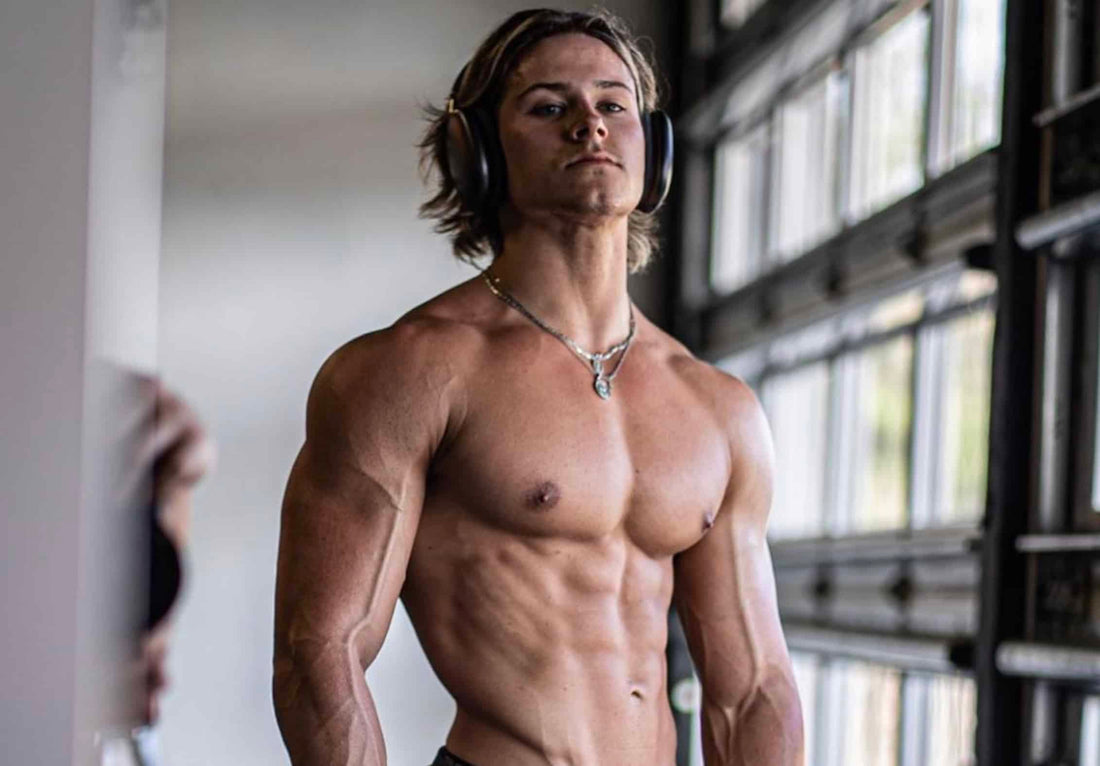 Alex Eubank posing shirtless in headphones inside a brightly lit gym