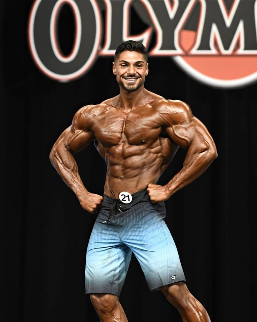 Andrei Deiu posing on the bodybuilding stage with defined arms, chest and shoulders