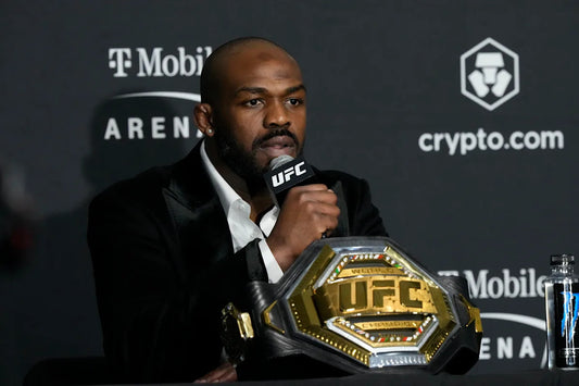 Jon Jones speaks at a UFC press conference beside a heavyweight championship belt in 2024.