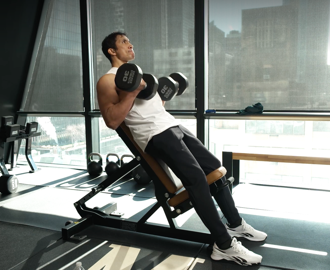 Man performing incline dumbbell curls while seated on an angled weight bench