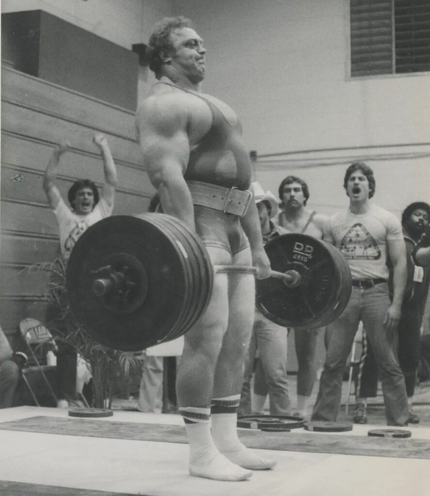 Bill Kazmaier locking out a heavily loaded barbell deadlift in a vintage powerlifting competition photograph