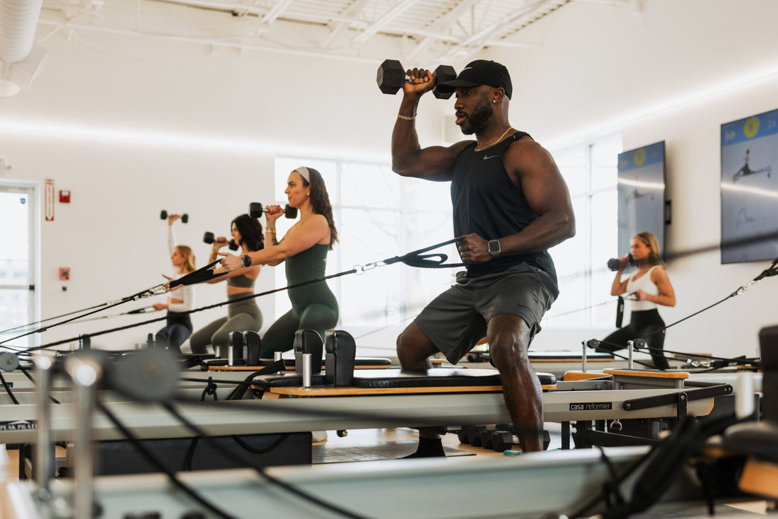 Muscular man holding a dumbbell during a group Reformer Pilates session