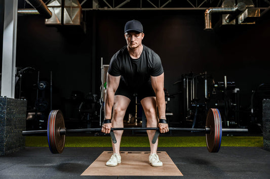 Male athlete preparing a loaded barbell deadlift on a gym platform, wearing a black shirt and cap