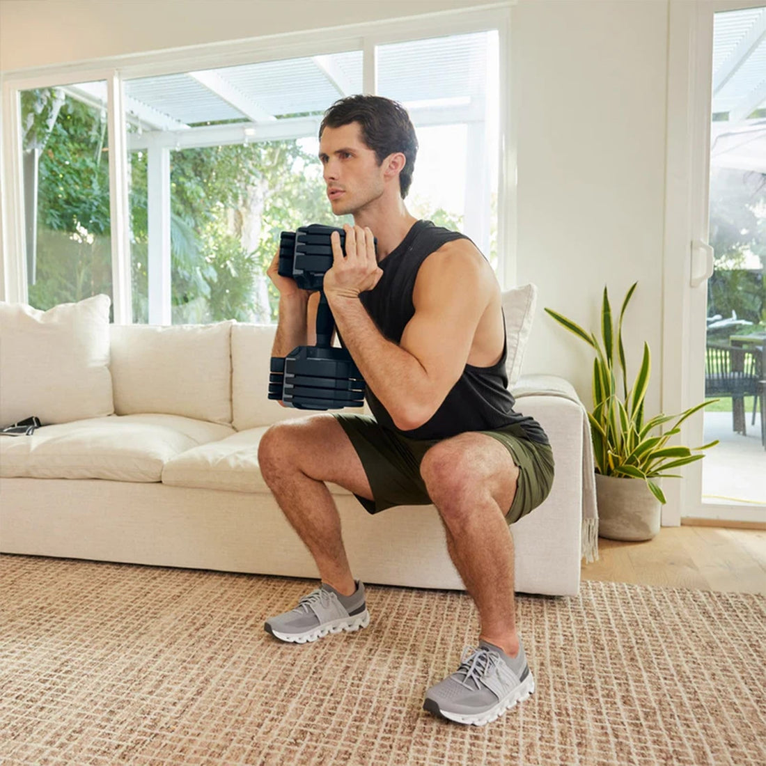 An athlete performing a controlled goblet squat with an adjustable dumbbell in a bright living room