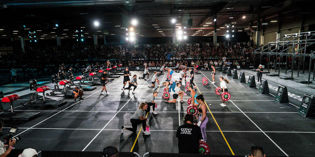 Functional fitness athletes competing on an indoor event floor with mixed strength and conditioning stations