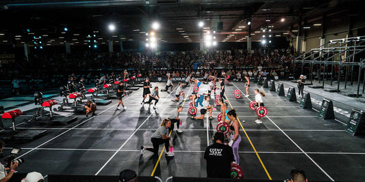 Functional fitness athletes competing on an indoor event floor with mixed strength and conditioning stations