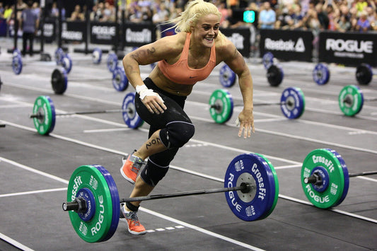 A CrossFit competitor sprinting between loaded barbells during a timed mixed-modal workout