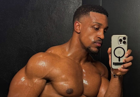 Ashton Hall smiling shirtless in a gym, showing muscular chest, shoulders and arms