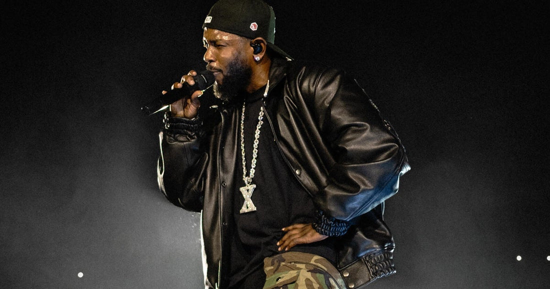 Kendrick Lamar performing into a microphone in a black leather jacket and camouflage pants