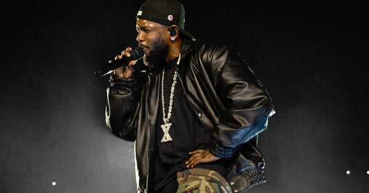 Kendrick Lamar performing into a microphone in a black leather jacket and camouflage pants