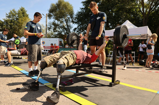 Veteran athlete with prosthetic legs bench pressing a loaded barbell at an earlier adaptive strength competition