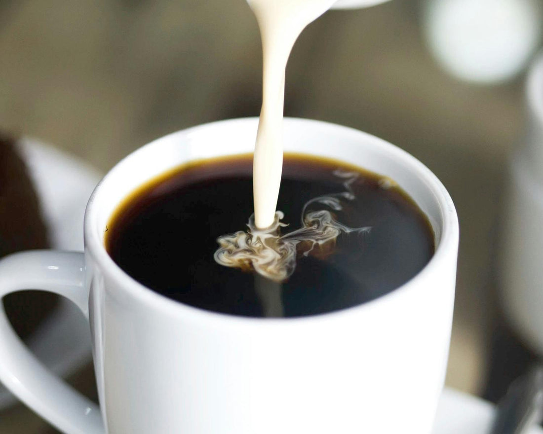White creamer being poured into black coffee in a white ceramic mug