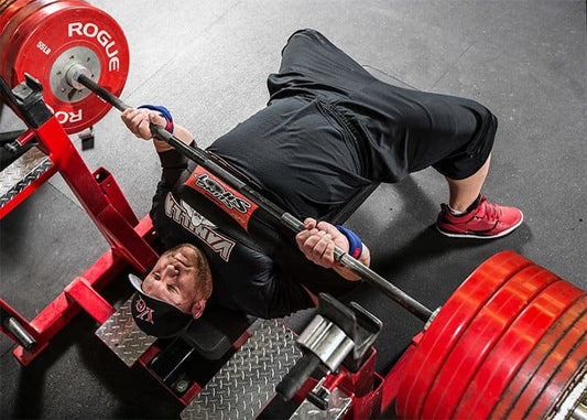 Eric Spoto performing a heavy hovering barbell bench press with red plates