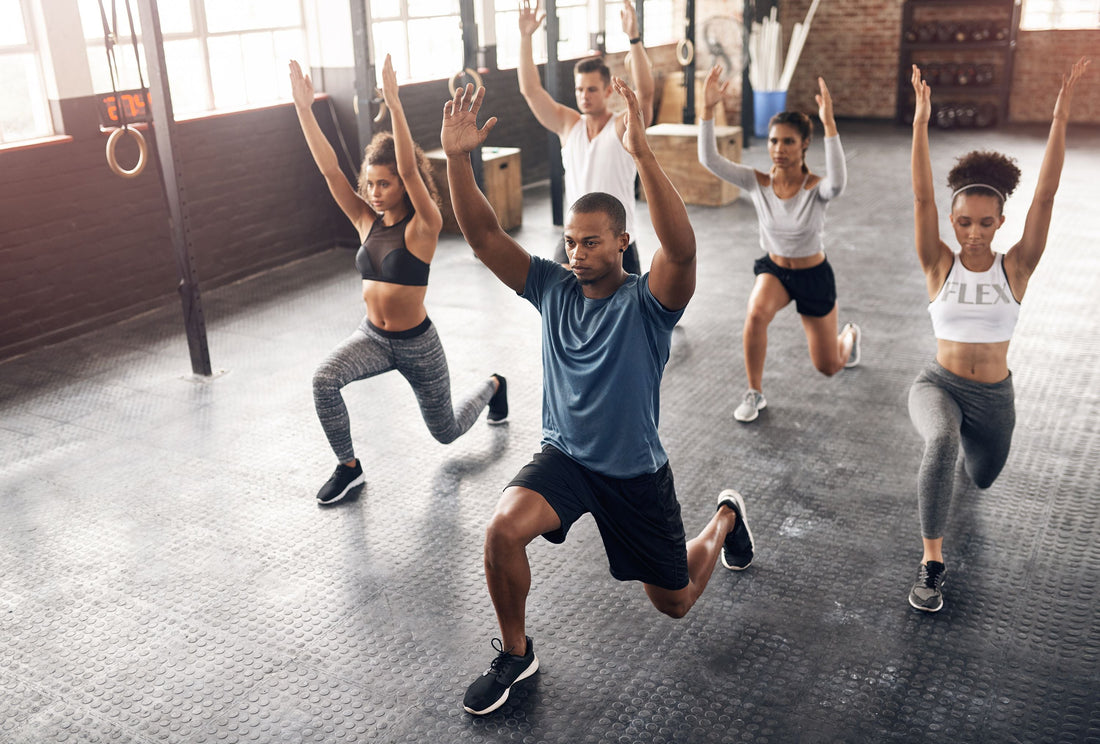 Group of gym athletes performing dynamic lunges with arms overhead during a mobility warm-up