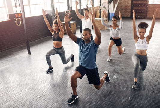 Group of gym athletes performing dynamic lunges with arms overhead during a mobility warm-up
