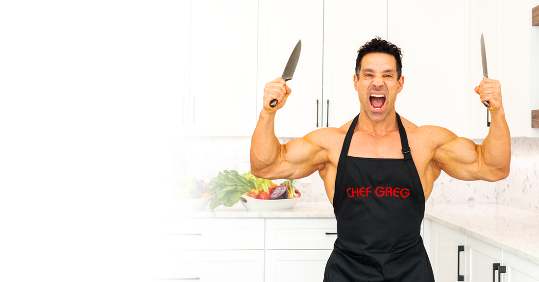 Greg Doucette in a black Chef Greg apron enthusiastically posing in a bright kitchen with vegetables